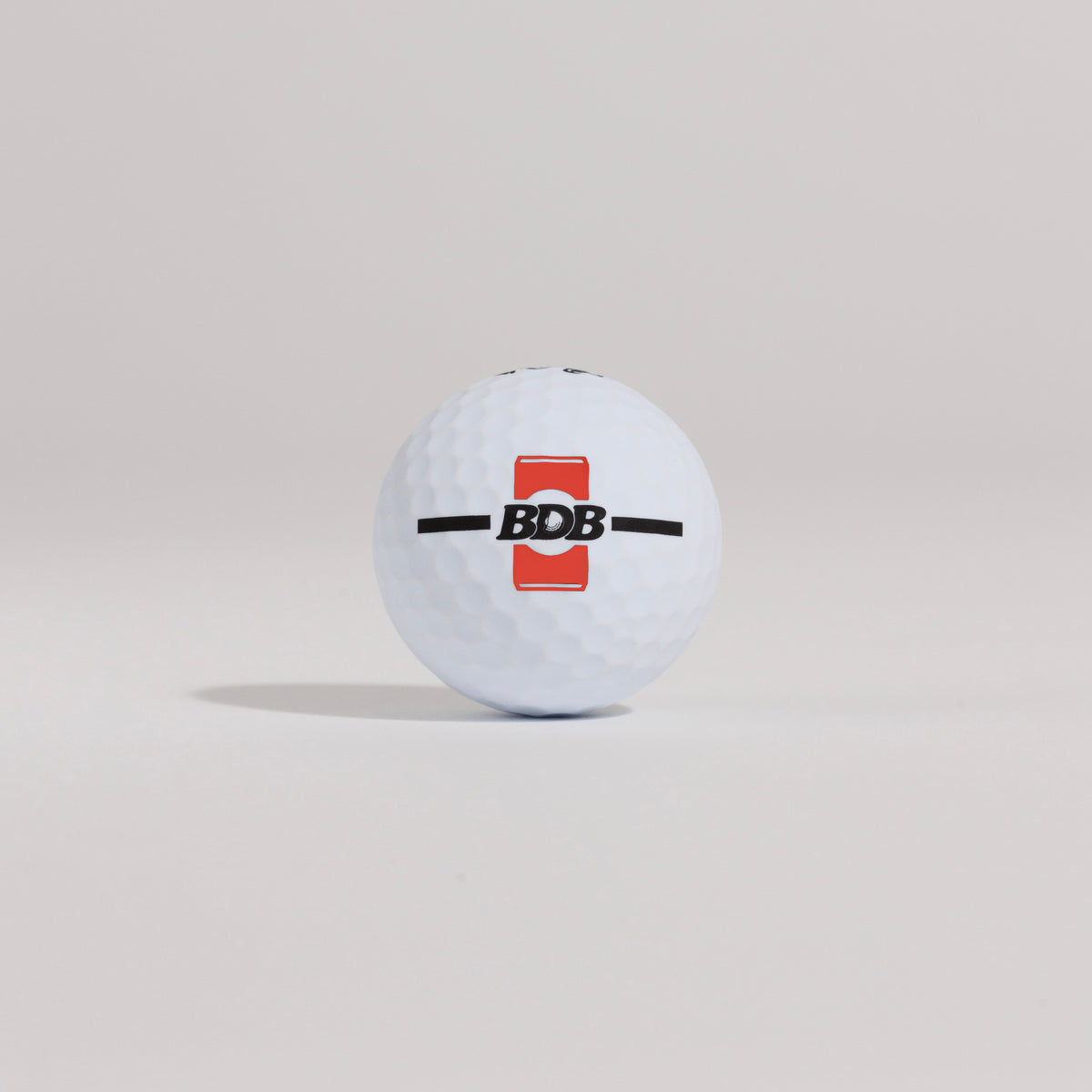 The Mulligan golf ball resting on a tee against a white background, showing BDB can putting and driving alignment tool