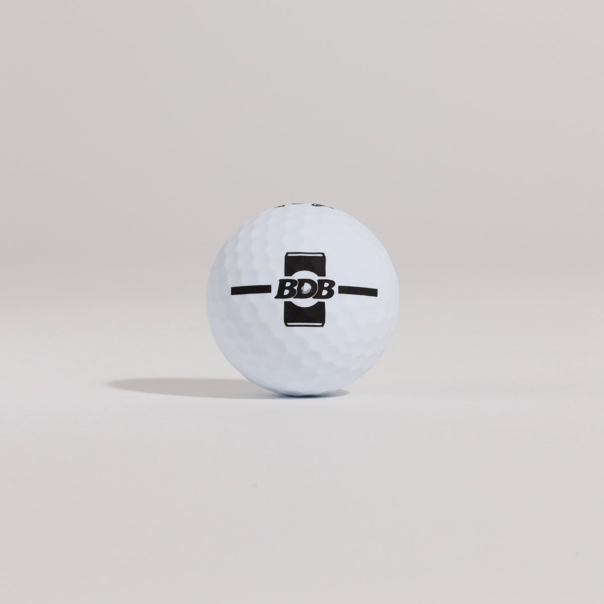 The Mulligan golf ball resting on a tee against a white background, showing BDB can putting and driving alignment tool
