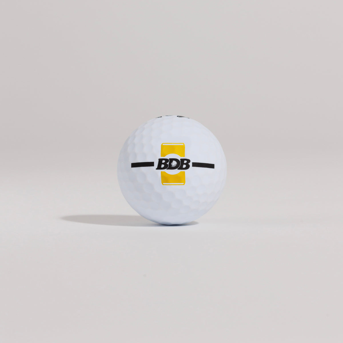The Mulligan golf ball resting on a tee against a white background, showing BDB can putting and driving alignment tool
