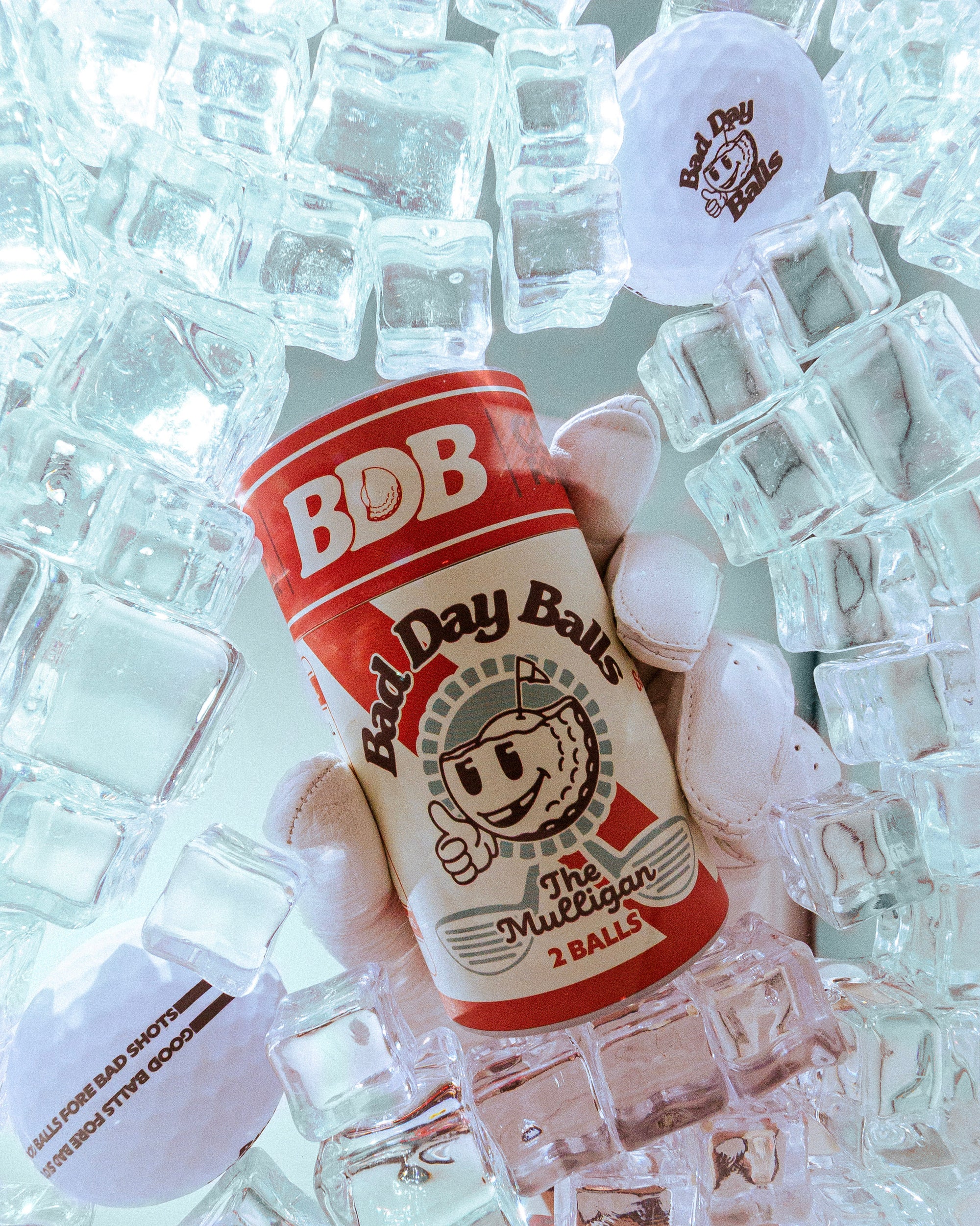 A can of BDB Bad Day Balls golf balls surrounded by clear ice cubes, with golf balls placed on and around it.