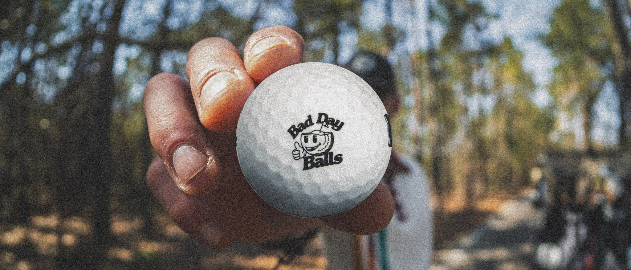 Golf ball with 'Bad Day Balls' logo held in a hand  on the course