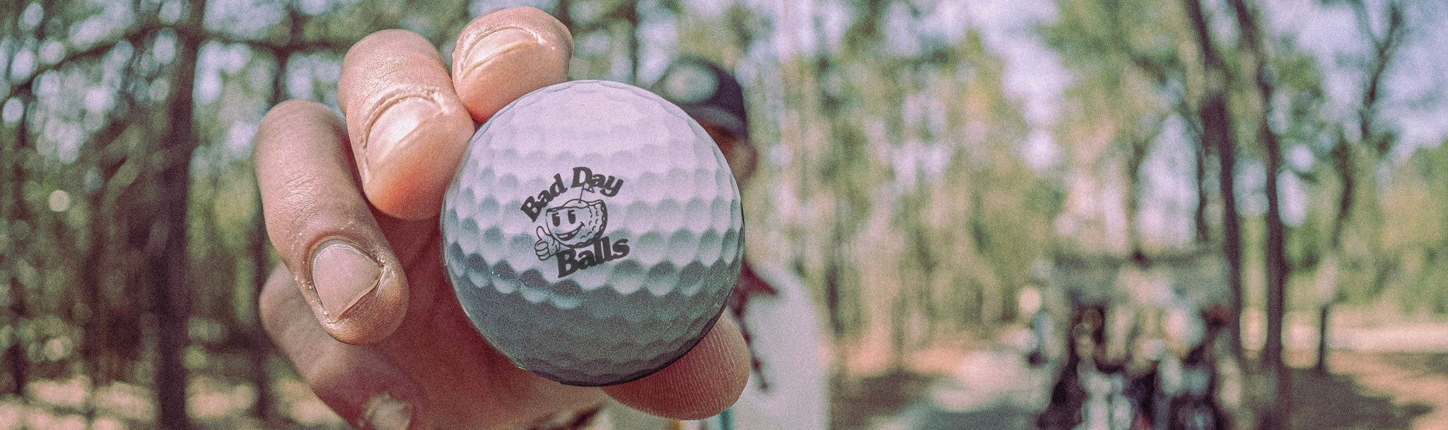 Golf ball with 'Bad Day Balls' logo held in a hand  on the course