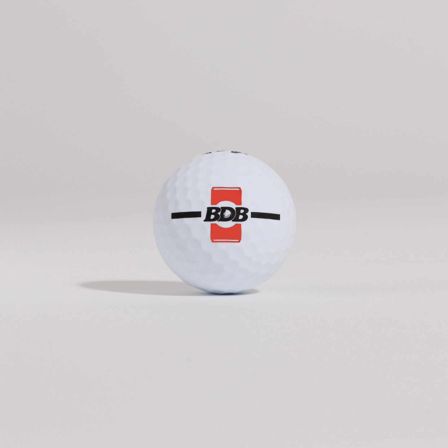 The Mulligan golf ball resting on a tee against a white background, showing BDB can putting and driving alignment tool