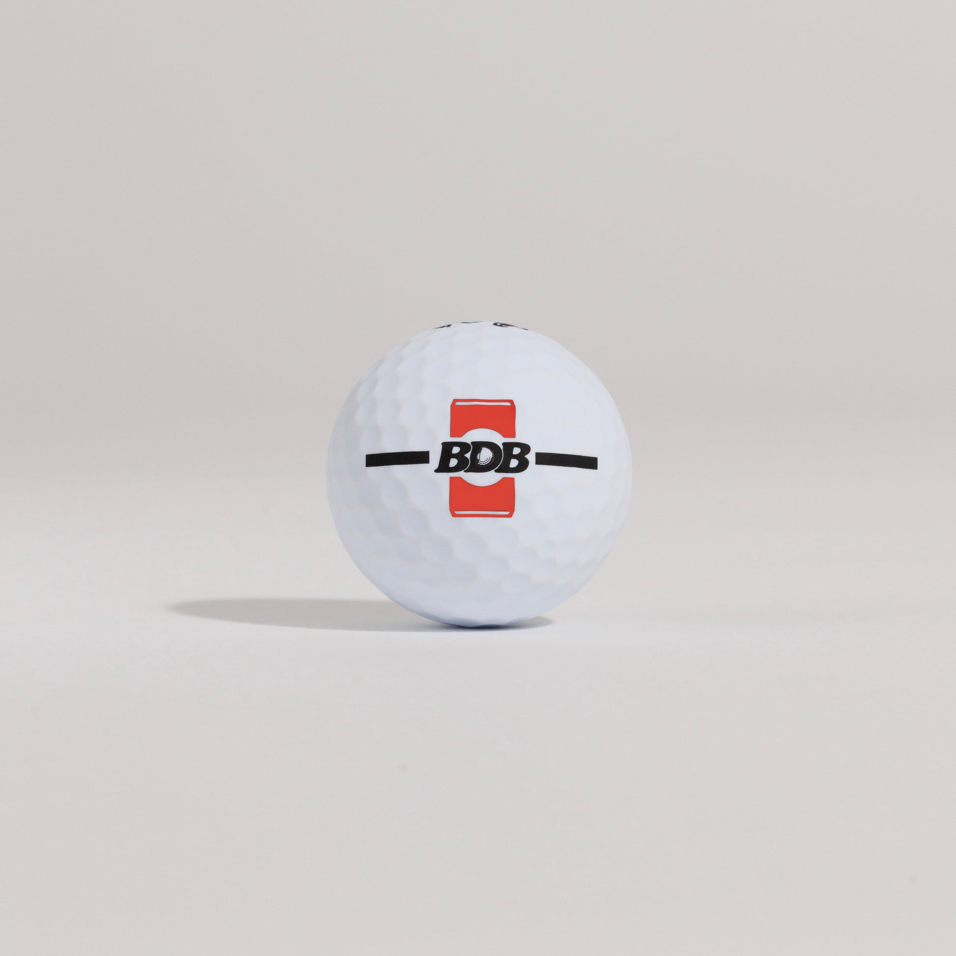 The Mulligan golf ball resting on a tee against a white background, showing BDB can putting and driving alignment tool