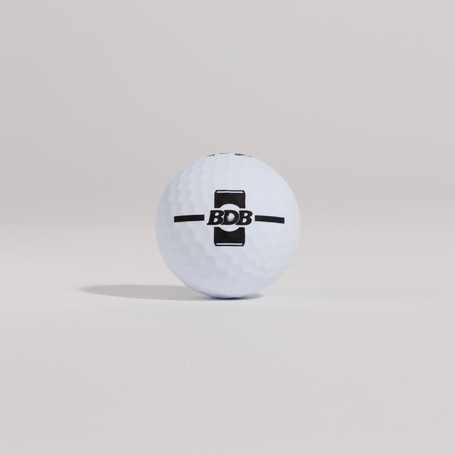 The Mulligan golf ball resting on a tee against a white background, showing BDB can putting and driving alignment tool 