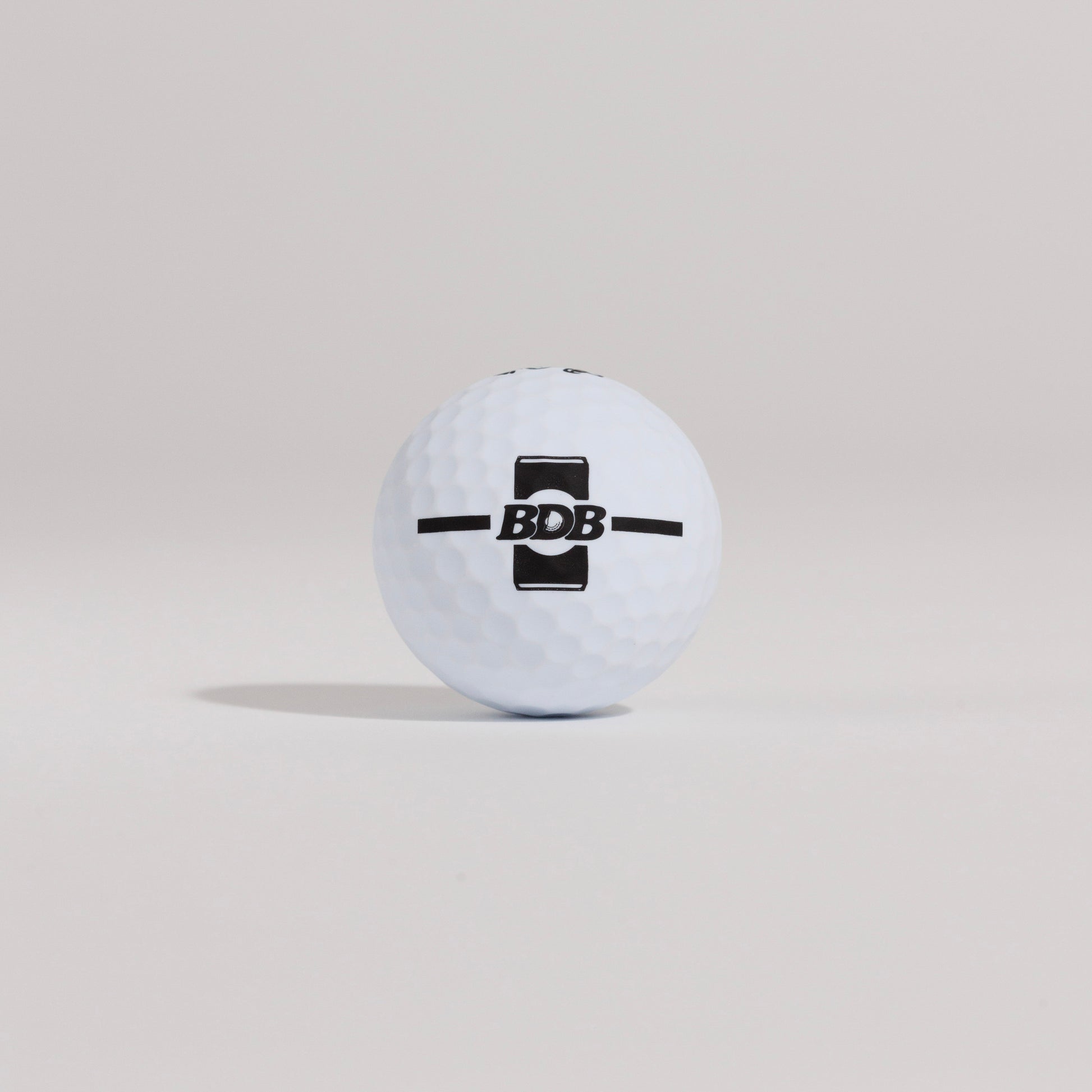 The Mulligan golf ball resting on a tee against a white background, showing BDB can putting and driving alignment tool 