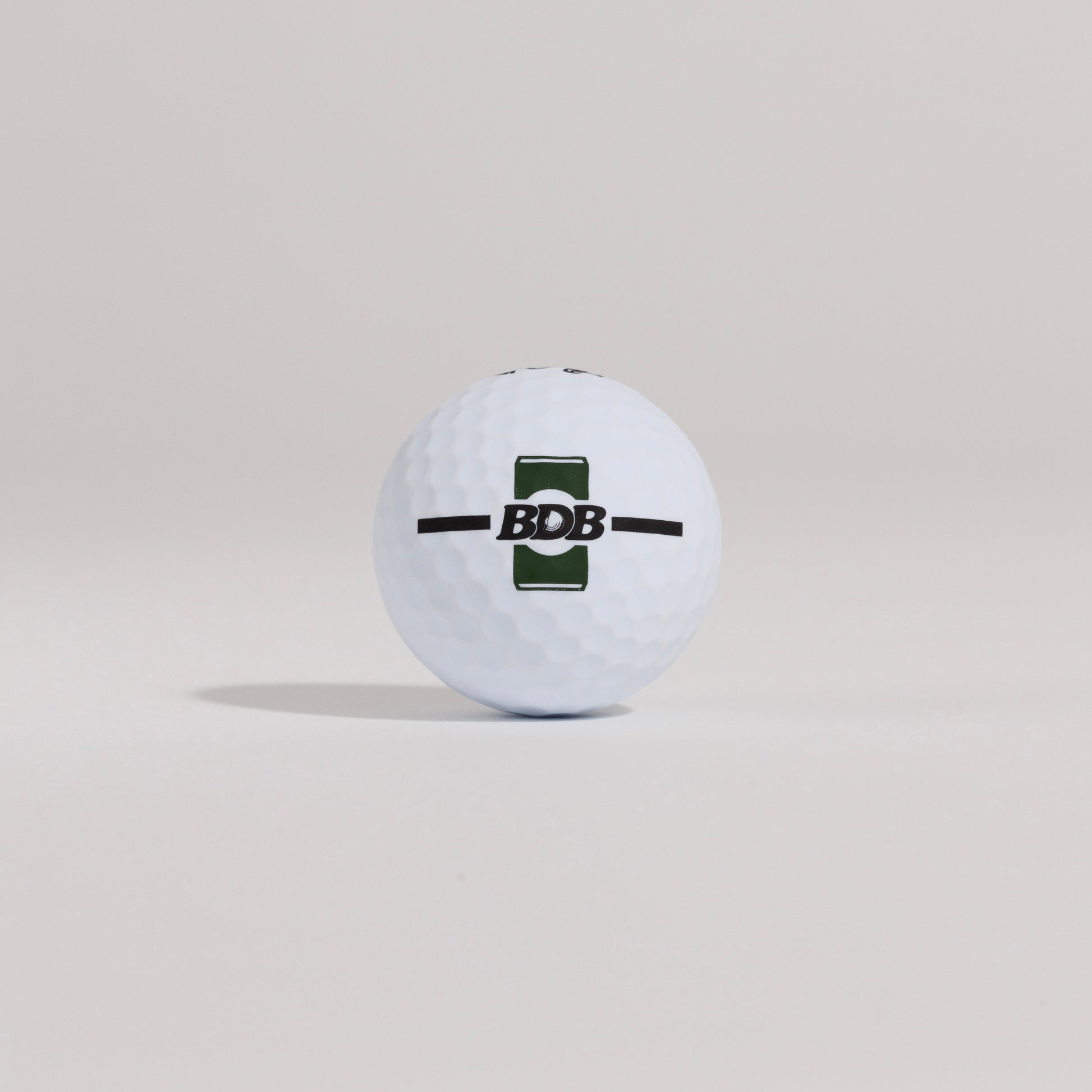 The Mulligan golf ball resting on a tee against a white background, showing BDB can putting and driving alignment tool