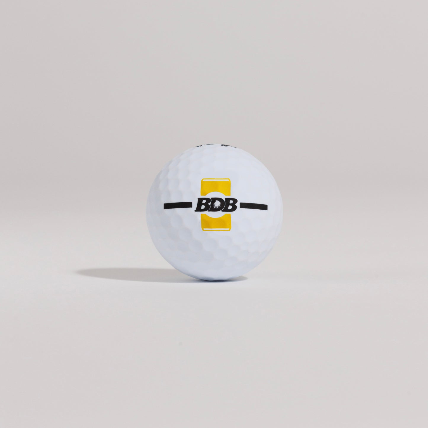 The Mulligan golf ball resting on a tee against a white background, showing BDB can putting and driving alignment tool