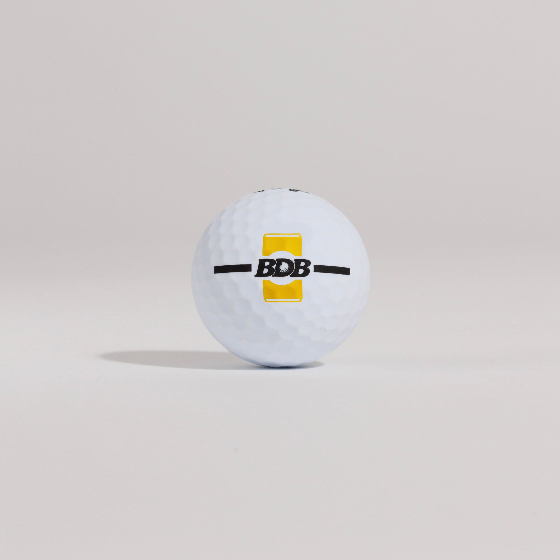 The Mulligan golf ball resting on a tee against a white background, showing BDB can putting and driving alignment tool