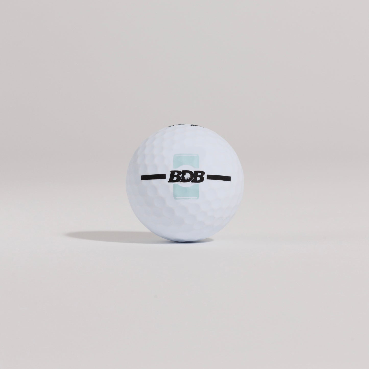 The Mulligan golf ball resting on a tee against a white background, showing BDB can putting and driving alignment tool