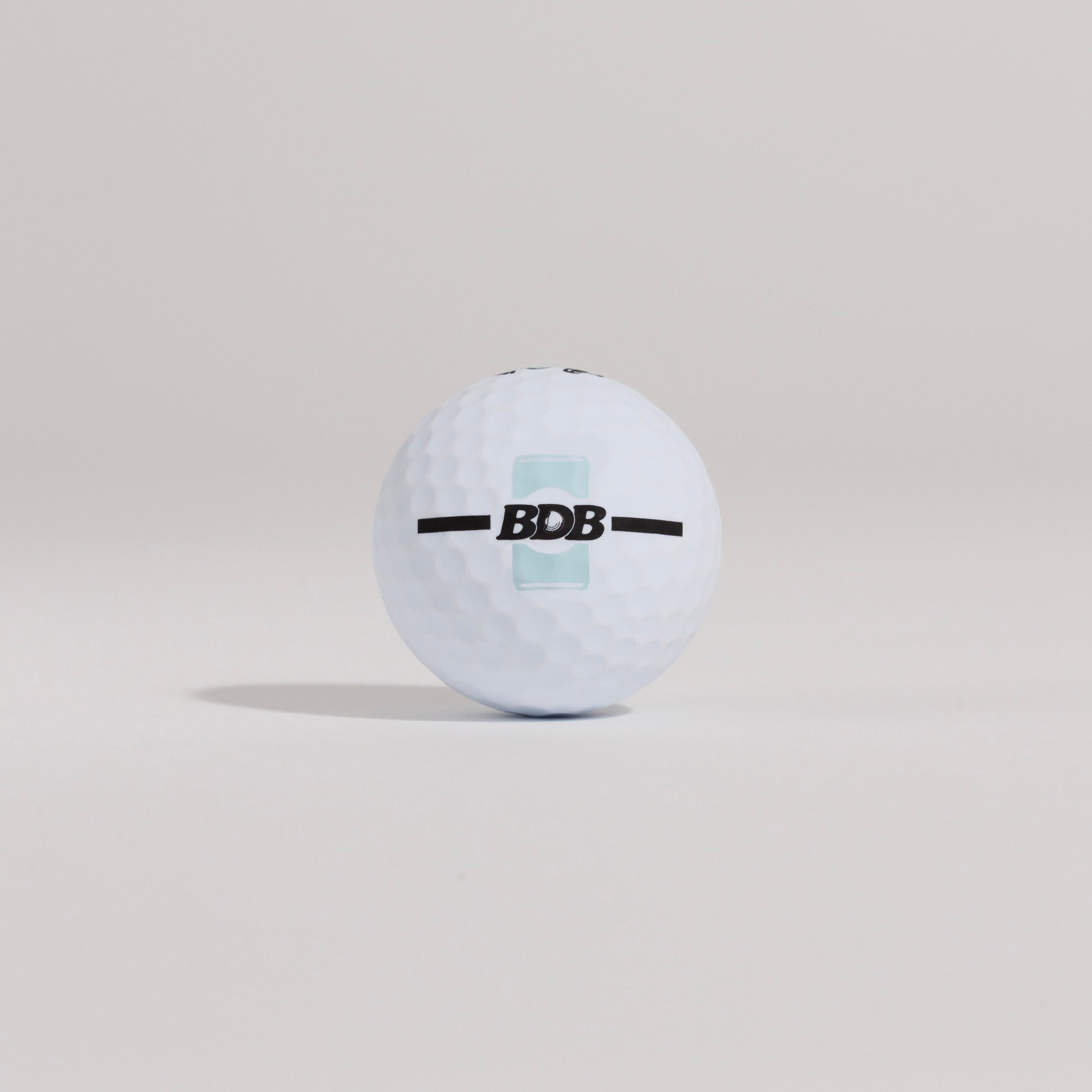 The Mulligan golf ball resting on a tee against a white background, showing BDB can putting and driving alignment tool