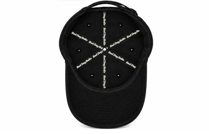 Black baseball cap shown from the back, featuring a black fabric back panel with multiple ventilation eyelets and white text printed in a starburst pattern reading 'Bad Dog Bitch'.